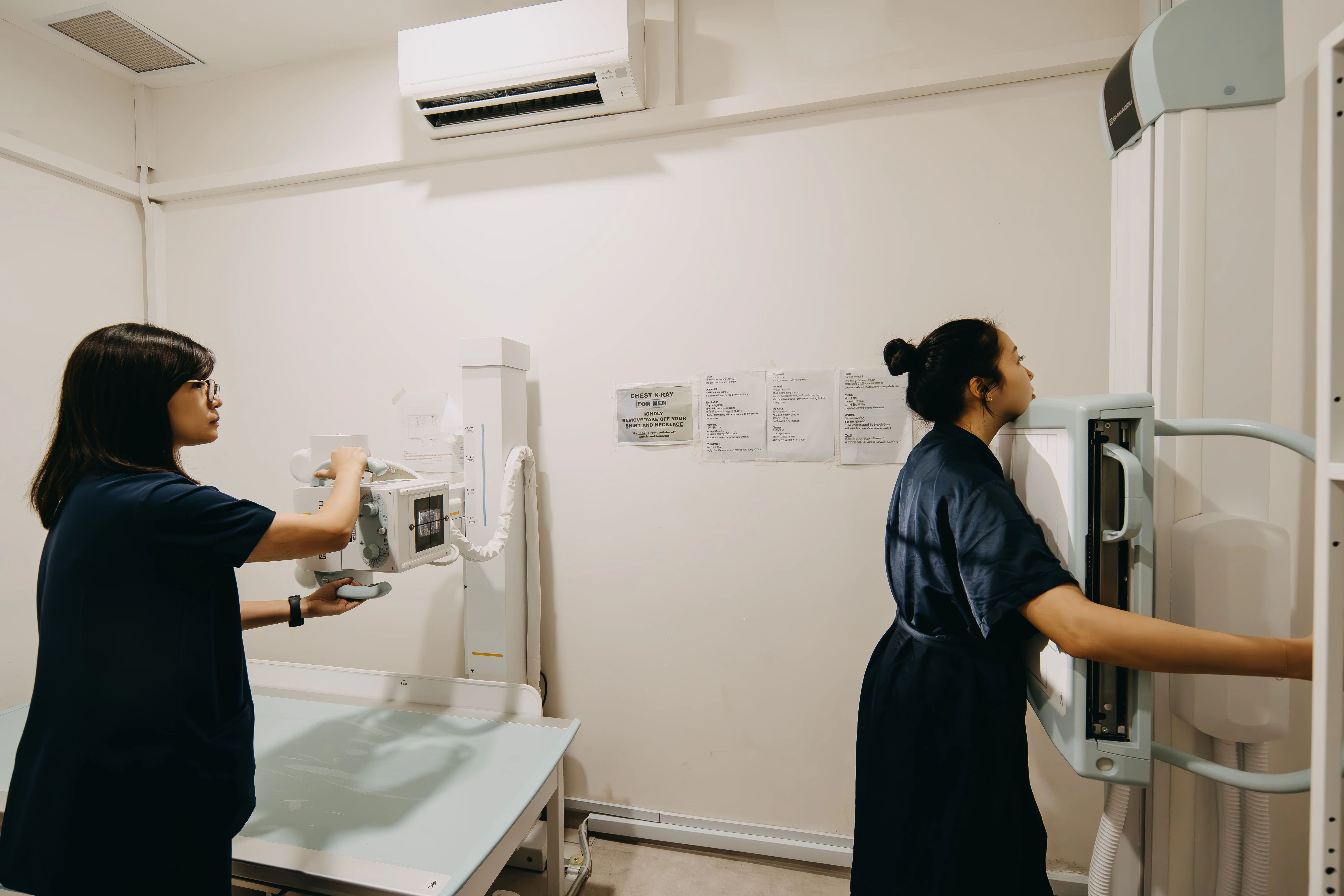 Radiographer operating the X-ray machine while a patient stands for a chest X-ray