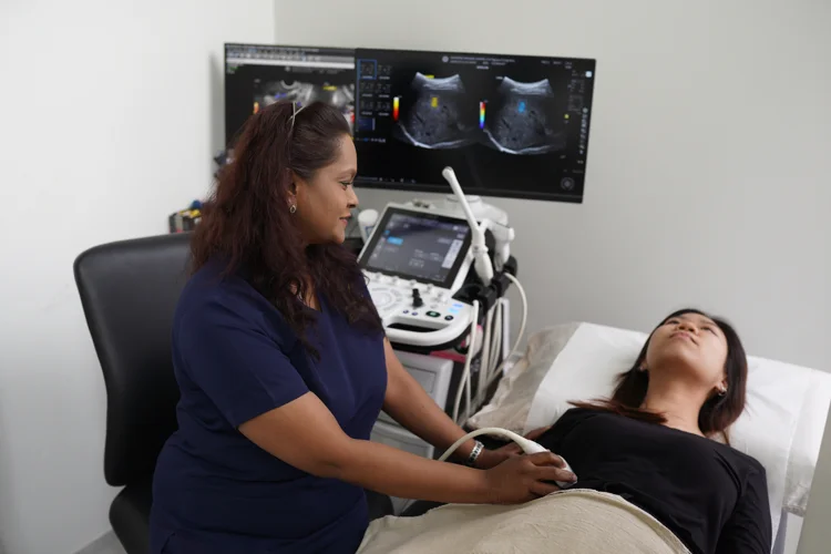 Female sonographer performing an ultrasound scan on a patient in a clinic room