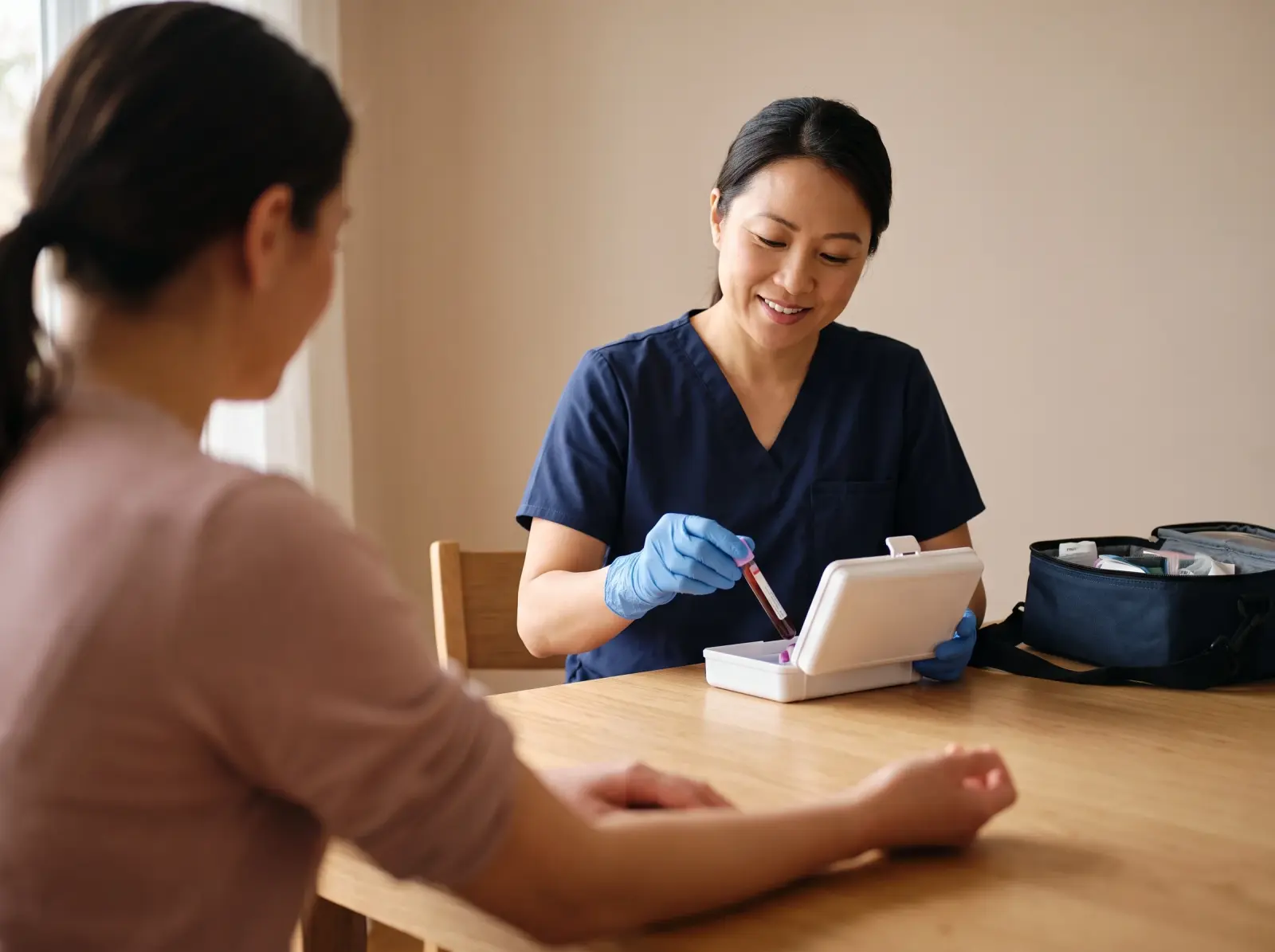 Nurse in navy scrubs placing a blood sample tube into a case at a dining table
