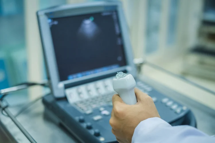 Sonographer holding an ultrasound transducer coated with gel beside the machine