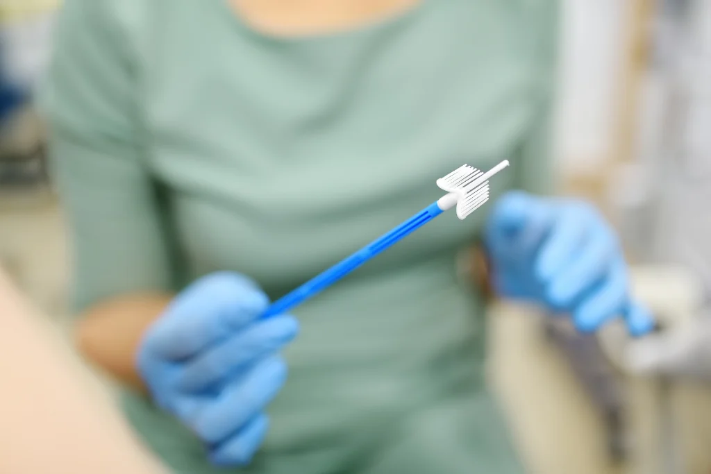 Healthcare worker holding cervical cell sampling brush and speculum used during pap smear procedure.