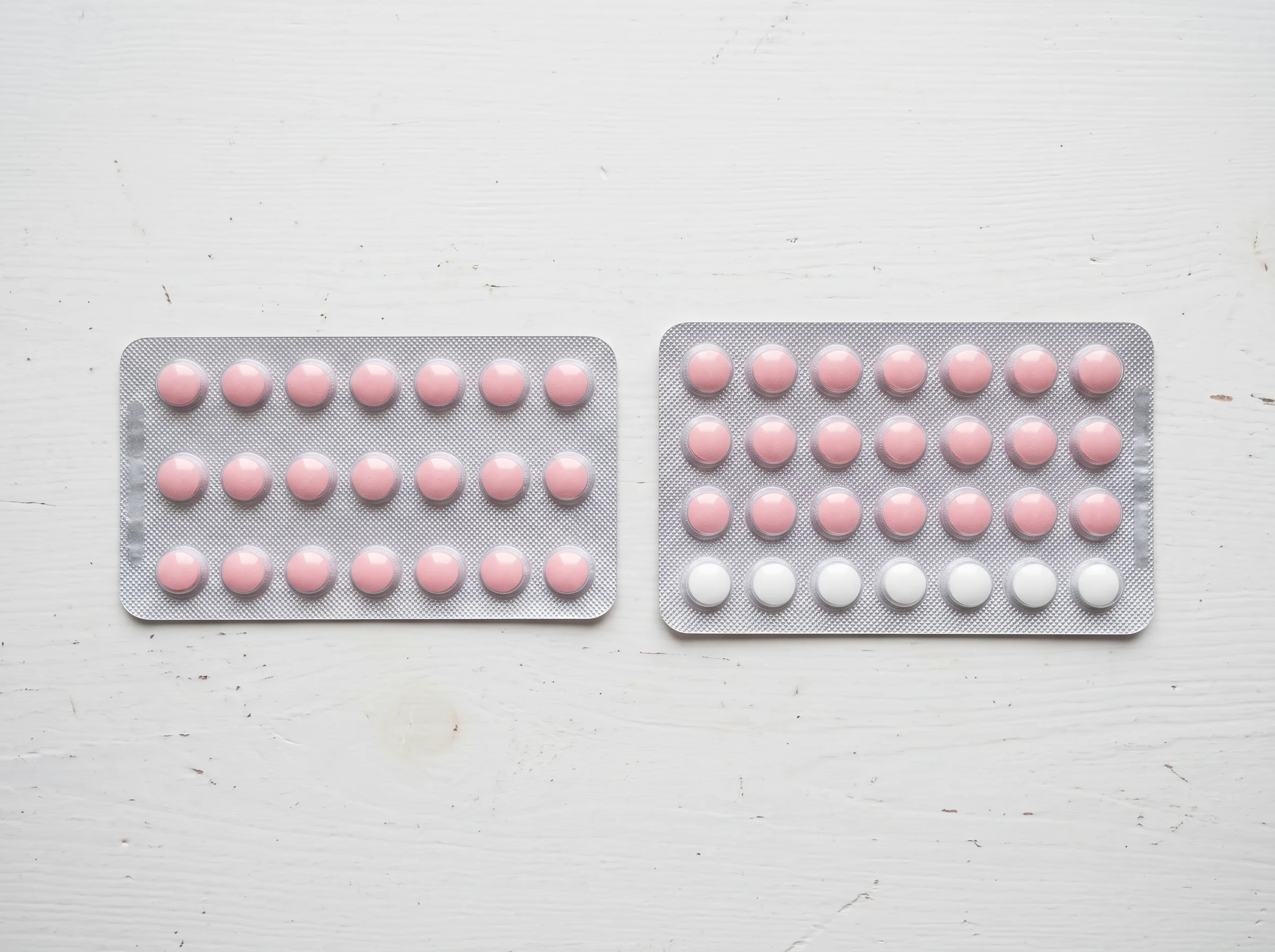 A 21-day and a 28-day pack of birth control pills side by side on a white table