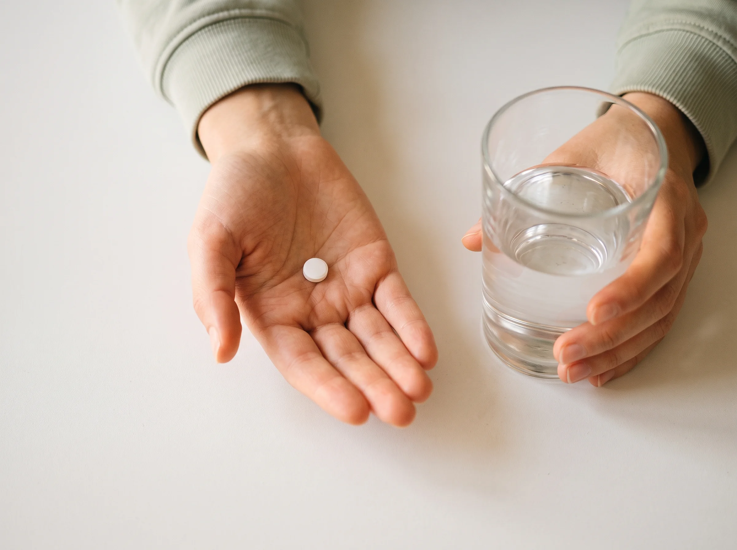 Morning-after pill in one open palm, the other hand holding a glass of water