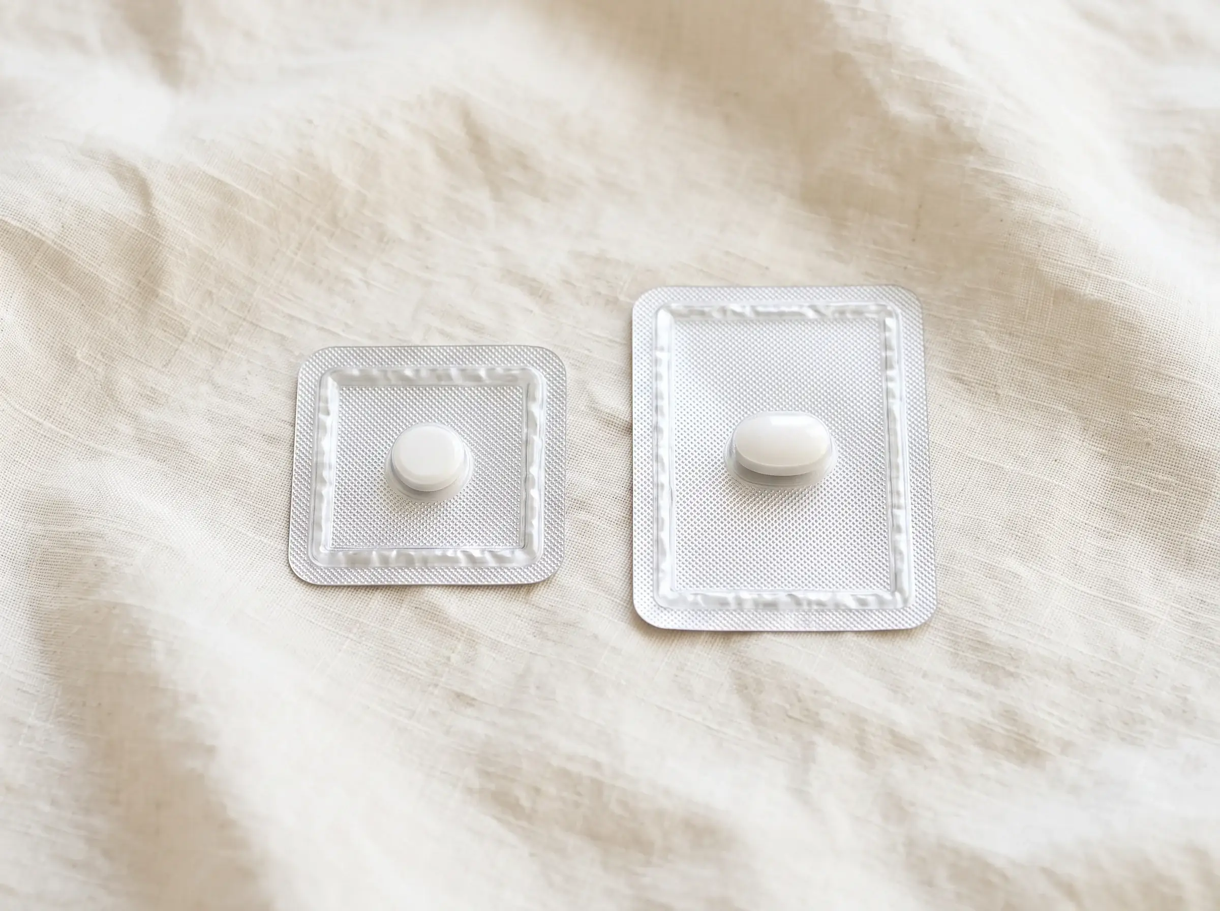 Two morning-after pill blister packs, each holding one tablet, on cream linen
