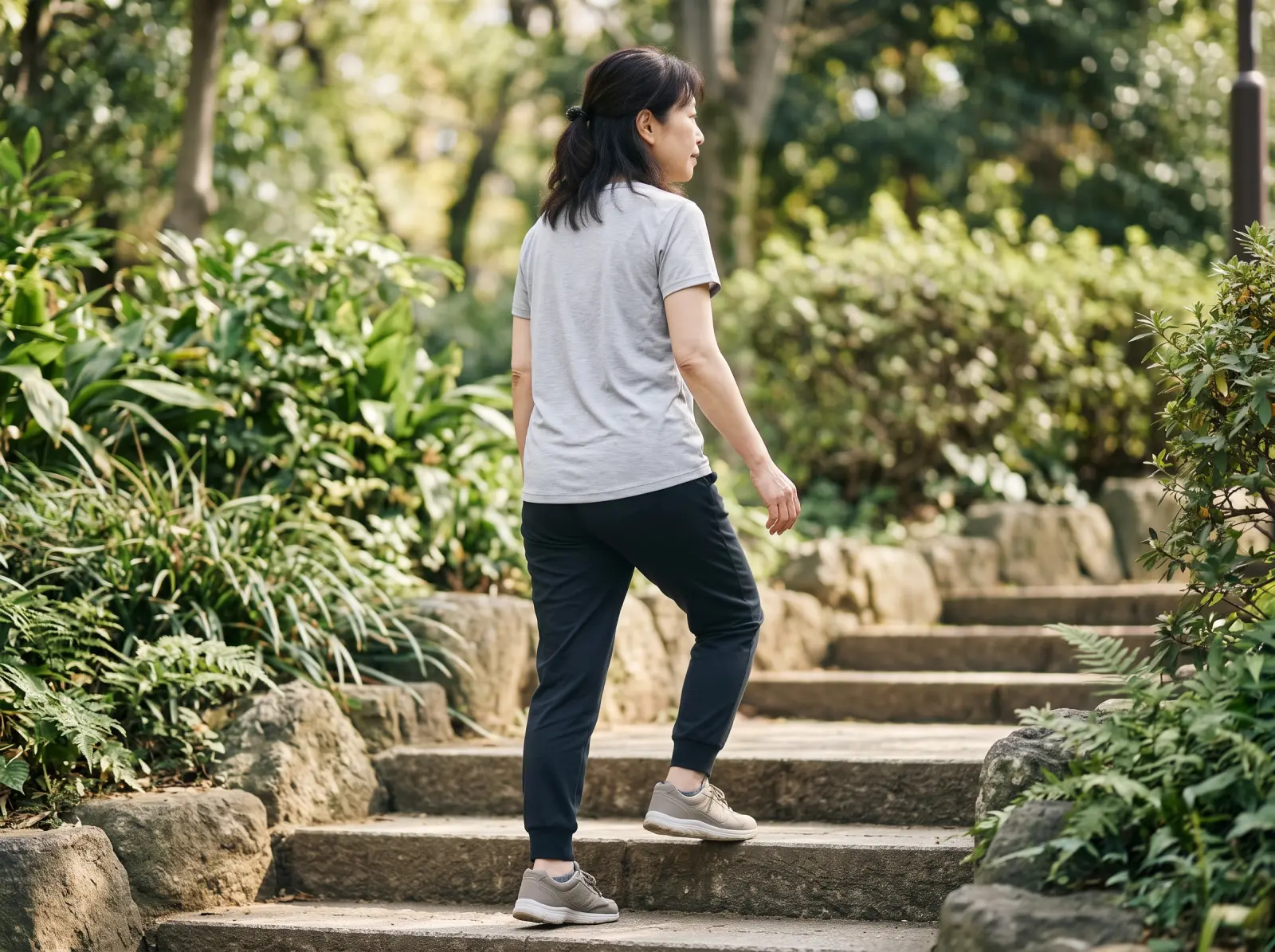 Woman in her fifties in a grey T-shirt walking up stone steps in a green park