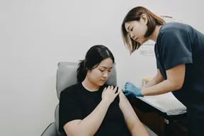 Woman receiving a vaccination in the upper arm from a female clinic staff member