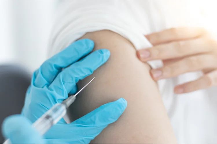 Doctor administering polio vaccine (IPV) into adult's upper arm during immunisation.