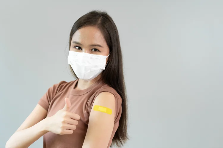 Woman wearing mask after receiving Pfizer-BioNTech COVID-19 JN.1 vaccine with plaster on arm.