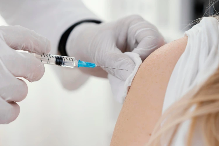 Doctor administering meningococcal vaccine injection in female patient’s upper arm before travel