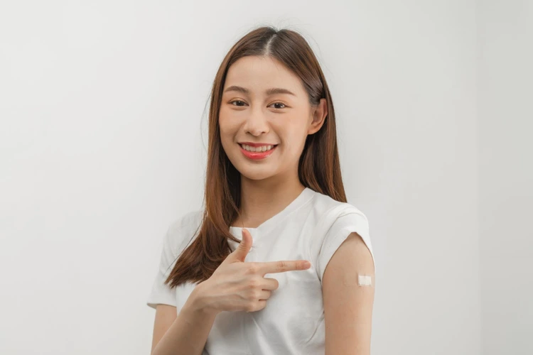 Young woman smiling and pointing at typhoid vaccine plaster on arm after vaccination.